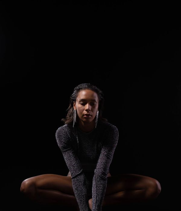 Woman in a graceful yoga pose in a serene, dark studio.